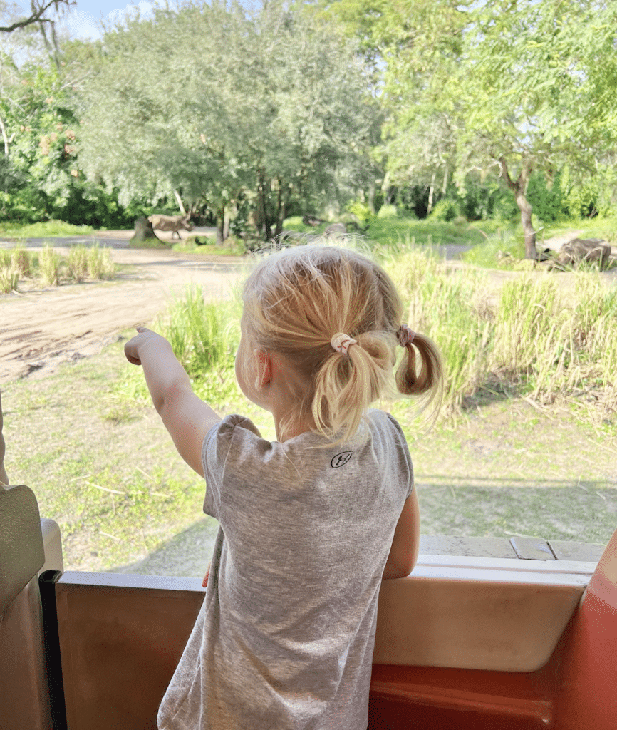 Young girl excitedly pointing out animals during a safari ride at Disney's Animal Kingdom.